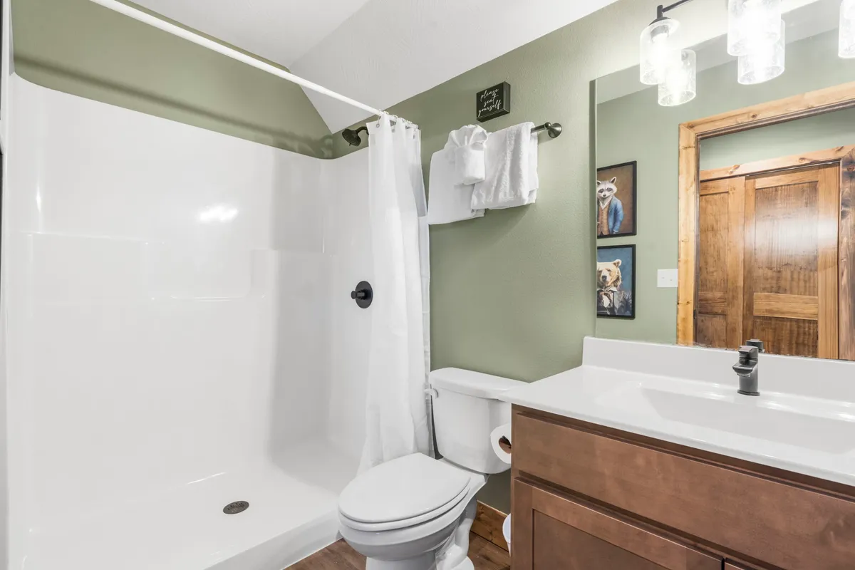 A modern bathroom interior featuring a spacious shower area, vanity, wooden door, and tasteful decorative artwork. The clean and calm atmosphere is perfect for relaxation and personal care after a day of outdoor activities.