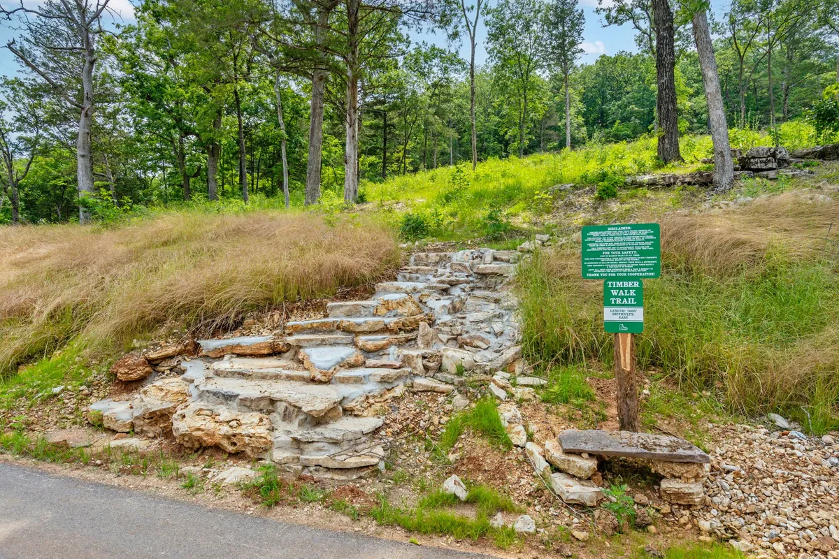 Stone steps lead into a lush, green wood, marked by a trail sign, inviting guests to explore the surrounding nature. The image radiates peacefulness and the appeal of morning or evening walks in the woods.