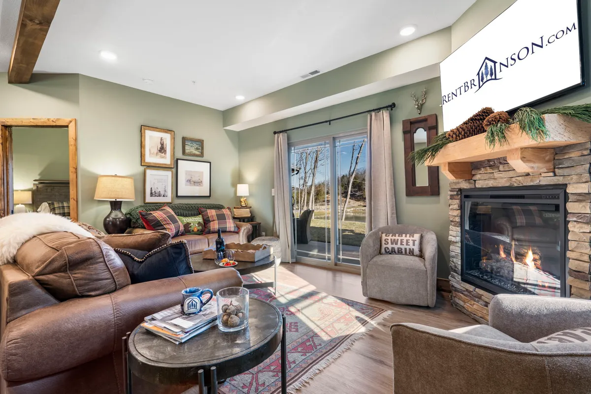 A spacious living area with a comfortable seating arrangement, a prominent fireplace, and large windows that frame outdoor views. Decorative artwork enhances the inviting, homely feel, while the natural light brightens the space, reinforcing the blend of nostalgia and modern comfort.