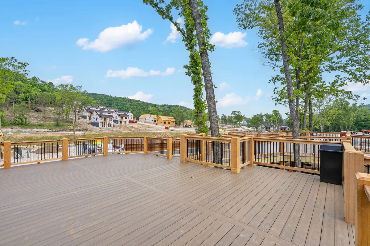 A spacious wooden deck surrounded by lush trees, with comfortable seating and a view of nearby houses, inviting guests to unwind, dine, or socialize while enjoying the natural landscape.