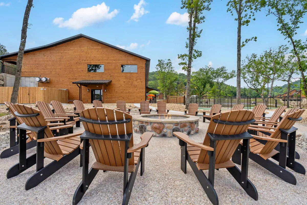 A cozy fire pit area with classic Adirondack chairs encircling the flames, set beside a wooden building and framed by towering trees, creating a gathering point for storytelling and s'mores.