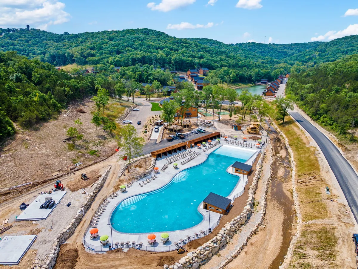A large outdoor swimming pool surrounded by greenery, cabana-style structures, and areas for barbecuing and social gatherings, conveying a vibrant and recreational resort atmosphere.