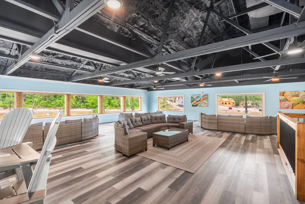 A comfortable and expansive sectional sofa faces a coffee table, with windows behind offering views of nature. Artwork on the walls and the inviting layout make this an ideal space for socializing, relaxing, or enjoying the changing daylight throughout the seasons.